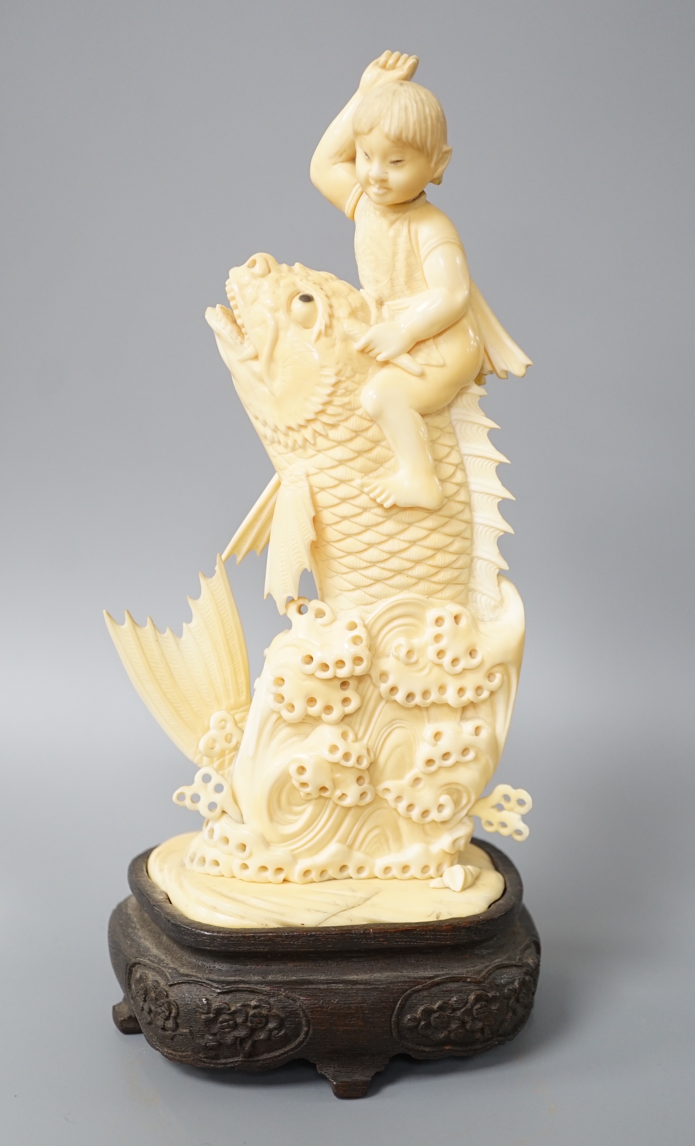 A Japanese sectional ivory okimono of a boy riding a leaping carp, early 20th century, wood stand, 25cm